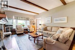 Living room featuring wood finished floors, beam ceiling, and a stone fireplace - 