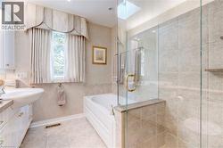 Bathroom with a skylight, a garden tub, vanity, a stall shower, and light tile patterned floors - 