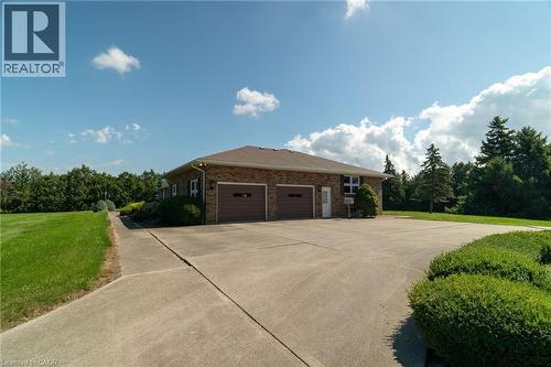 View of side of property featuring brick siding, an attached garage, a lawn, and driveway - 6828 Third Line, Chatham, ON 