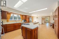 Kitchen with light floors, brown cabinets, light countertops, a center island with sink, and stainless steel appliances - 