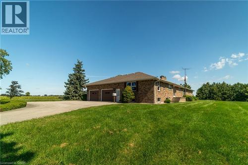 View of side of property featuring concrete driveway, brick siding, a lawn, a chimney, and an attached garage - 6828 Third Line, Chatham, ON - Outdoor