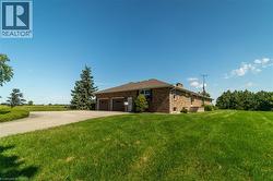 View of side of property featuring concrete driveway, brick siding, a lawn, a chimney, and an attached garage - 