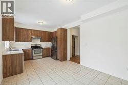 Kitchen featuring light countertops, appliances with stainless steel finishes, light tile patterned floors, under cabinet range hood, and brown cabinets - 