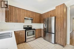 Kitchen with stainless steel appliances, modern cabinets, brown cabinets, under cabinet range hood, and light tile patterned flooring - 
