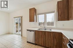 Kitchen featuring stainless steel dishwasher, brown cabinets, light countertops, and healthy amount of natural light - 