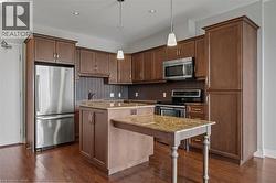 Kitchen with appliances with stainless steel finishes, a kitchen island, dark wood-style flooring, tasteful backsplash, and recessed lighting - 