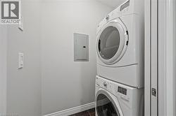 Laundry room featuring stacked washer / drying machine, electric panel, and dark tile patterned flooring - 