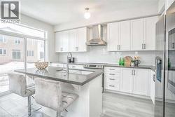 Kitchen featuring white cabinetry, appliances with stainless steel finishes, wall chimney exhaust hood, and tasteful backsplash - 