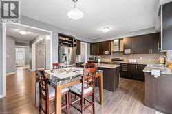 Kitchen with dark brown cabinets, a kitchen island, appliances with stainless steel finishes, backsplash, and wall chimney range hood - 