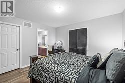 Bedroom with a textured ceiling, dark wood-type flooring, and connected bathroom - 