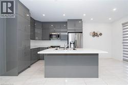 Kitchen with gray cabinetry, modern cabinets, appliances with stainless steel finishes, a center island with sink, and recessed lighting - 