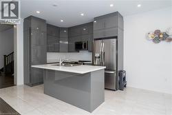Kitchen featuring gray cabinets, appliances with stainless steel finishes, modern cabinets, a center island with sink, and recessed lighting - 