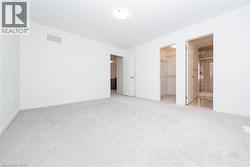 Unfurnished bedroom featuring ensuite bath, a walk in closet, and light carpet - 
