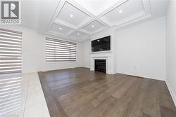 Unfurnished living room with coffered ceiling, a glass covered fireplace, light wood finished floors, beam ceiling, and recessed lighting - 