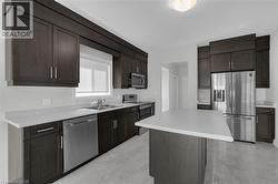 Kitchen with stainless steel appliances, dark brown cabinets, light countertops, a kitchen island, and light marble finish floors - 