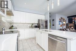 Kitchen featuring stainless steel appliances, a sink, light tile patterned flooring, decorative backsplash, and white cabinetry - 