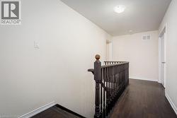 Hallway featuring dark wood-style floors, baseboards, visible vents, and an upstairs landing - 