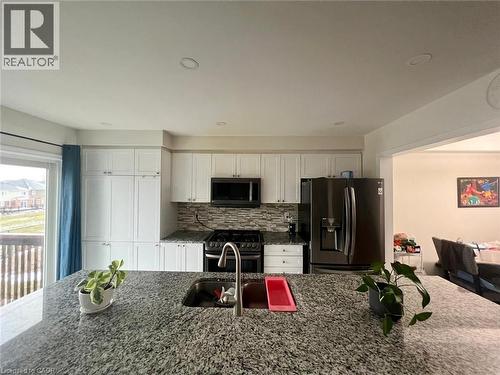 Kitchen featuring dark stone countertops, appliances with stainless steel finishes, white cabinetry, backsplash, and recessed lighting - 128 Watermill Street, Kitchener, ON - Indoor Photo Showing Kitchen With Double Sink