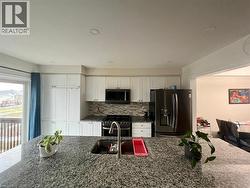 Kitchen featuring dark stone countertops, appliances with stainless steel finishes, white cabinetry, backsplash, and recessed lighting - 