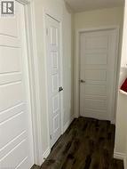 Hallway featuring dark wood-type flooring and baseboards - 