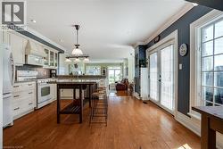 Kitchen with glass insert cabinets, white appliances, pendant lighting, white cabinetry, and ornamental molding - 