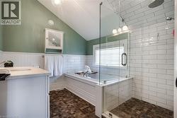 Full bathroom featuring vanity, a wainscoted wall, vaulted ceiling, a stall shower, and a bath - 
