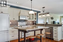 Kitchen with a kitchen breakfast bar, white appliances, pendant lighting, crown molding, and glass insert cabinets - 