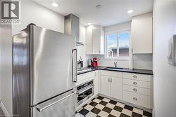 Kitchen featuring light flooring, stainless steel appliances, dark countertops, white cabinetry, and wall chimney range hood - 