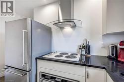 Kitchen featuring white cabinetry, island exhaust hood, appliances with stainless steel finishes, and dark stone countertops - 