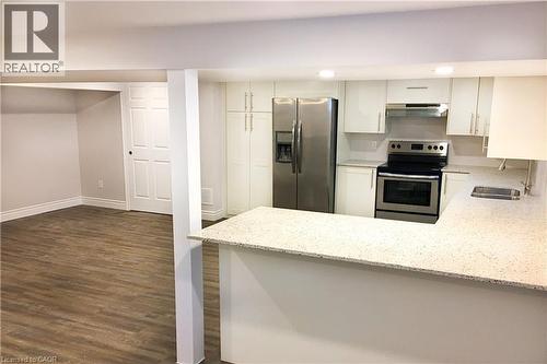 Kitchen featuring appliances with stainless steel finishes, light stone counters, a peninsula, dark wood finished floors, and under cabinet range hood - 557 Lake Street, St. Catharines, ON - Indoor Photo Showing Kitchen