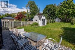 Fenced backyard with a storage shed, a patio area, outdoor dining area, and view of scattered trees - 
