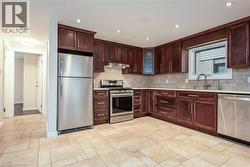Kitchen with stainless steel appliances, decorative backsplash, recessed lighting, light stone countertops, and dark brown cabinets - 