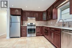 Kitchen featuring stainless steel appliances, glass insert cabinets, decorative backsplash, recessed lighting, and light stone countertops - 