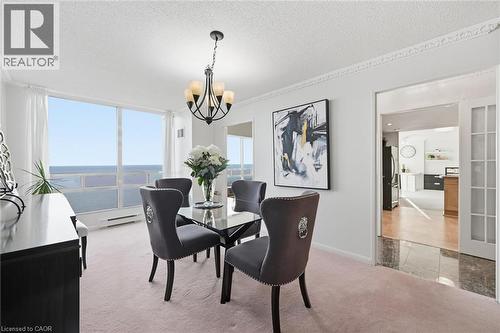 Dining area featuring light carpet, a textured ceiling, a chandelier, baseboard heating, and a water view - 2170 Marine Drive Unit# 1808, Oakville, ON - Indoor Photo Showing Dining Room