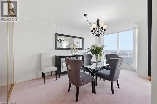Dining area featuring carpet floors, a chandelier, a water view, a textured ceiling, and ornamental molding - 2170 Marine Drive Unit# 1808, Oakville, ON - Indoor Photo Showing Dining Room