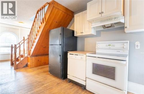 Kitchen with white appliances, light countertops, light wood-style flooring, under cabinet range hood, and a textured ceiling - 219 Erie Avenue, Brantford, ON - Indoor Photo Showing Kitchen
