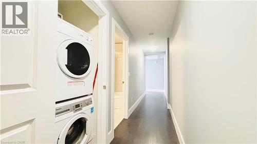 Laundry room featuring stacked washing machine and dryer and dark wood-style flooring - 155 St. Leger Unit# 107, Kitchener, ON - Indoor Photo Showing Laundry Room