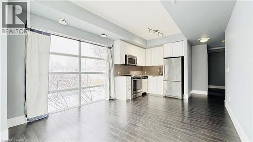 Kitchen with stainless steel appliances, white cabinets, dark wood-type flooring, track lighting, and backsplash - 155 St. Leger Unit# 107, Kitchener, ON - Indoor Photo Showing Kitchen