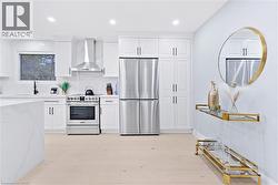 Kitchen with appliances with stainless steel finishes, wall chimney range hood, white cabinetry, recessed lighting, and tasteful backsplash - 