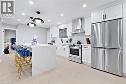 Kitchen featuring stainless steel appliances, wall chimney range hood, white cabinets, a breakfast bar, and a kitchen island - 