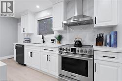 Kitchen featuring stainless steel electric stove, wall chimney exhaust hood, light stone counters, dishwasher, and white cabinetry - 