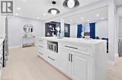 Kitchen with white cabinets, light stone counters, recessed lighting, an island with sink, and stainless steel microwave - 