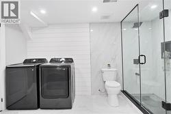 Bathroom with a marble finish shower, marble tiled flooring, washing machine and dryer, and recessed lighting - 