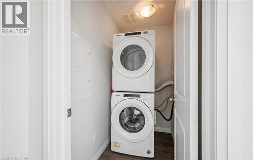 Washroom featuring electric panel, stacked washer / dryer, and wood finished floors - 24 Morrison Road Unit# D9, Kitchener, ON - Indoor Photo Showing Laundry Room