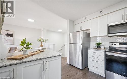 Kitchen featuring stainless steel appliances, white cabinets, light stone counters, dark wood-style floors, and tasteful backsplash - 24 Morrison Road Unit# D9, Kitchener, ON - Indoor Photo Showing Kitchen With Upgraded Kitchen