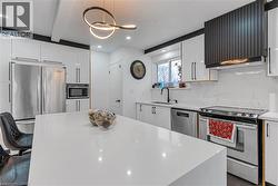 Kitchen with appliances with stainless steel finishes, white cabinets, ventilation hood, light stone countertops, and tasteful backsplash - 