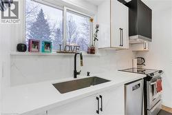 Kitchen with white cabinetry, appliances with stainless steel finishes, wall chimney exhaust hood, tasteful backsplash, and light stone counters - 