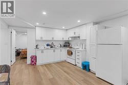 Kitchen featuring white appliances, white cabinetry, light countertops, light wood-type flooring, and recessed lighting - 