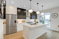 Kitchen with light wood-style floors, stainless steel fridge with ice dispenser, wall chimney exhaust hood, a sink, and a center island with sink - 