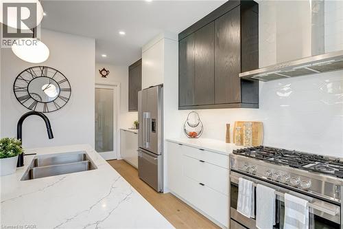 Kitchen featuring tasteful backsplash, wall chimney range hood, light wood-style floors, stainless steel appliances, and a sink - 151C Port Robinson Road, Pelham, ON - Indoor Photo Showing Kitchen With Double Sink With Upgraded Kitchen
